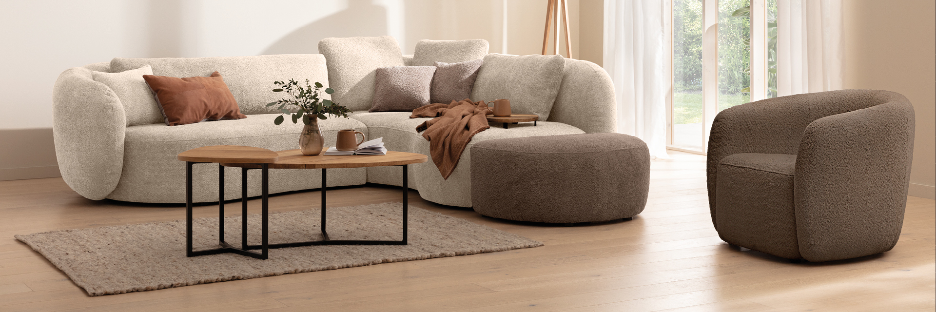 Helles Sofa mit Hocker, Sessel, Couchtischen, Teppich und Kissen vor Fensterfront