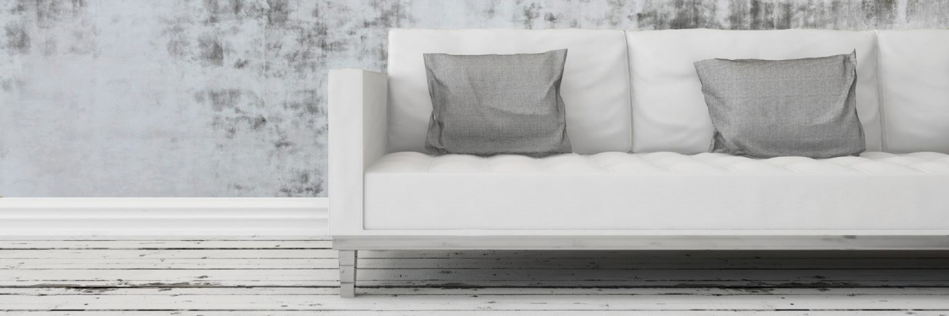 Weißes Sofa mit zwei grauen Kissen vor grauer Wand auf weißem Holzboden